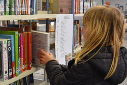 Mädchen zieht Buch aus dem Regal in der Schulbibliothek